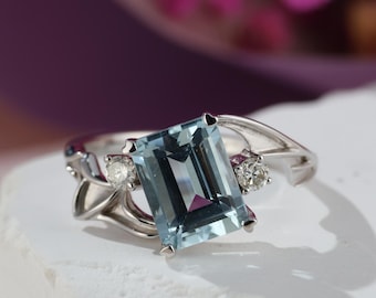 May include: A silver ring with a light blue aquamarine gemstone and two smaller diamonds. The ring has a delicate, vine-like design.
