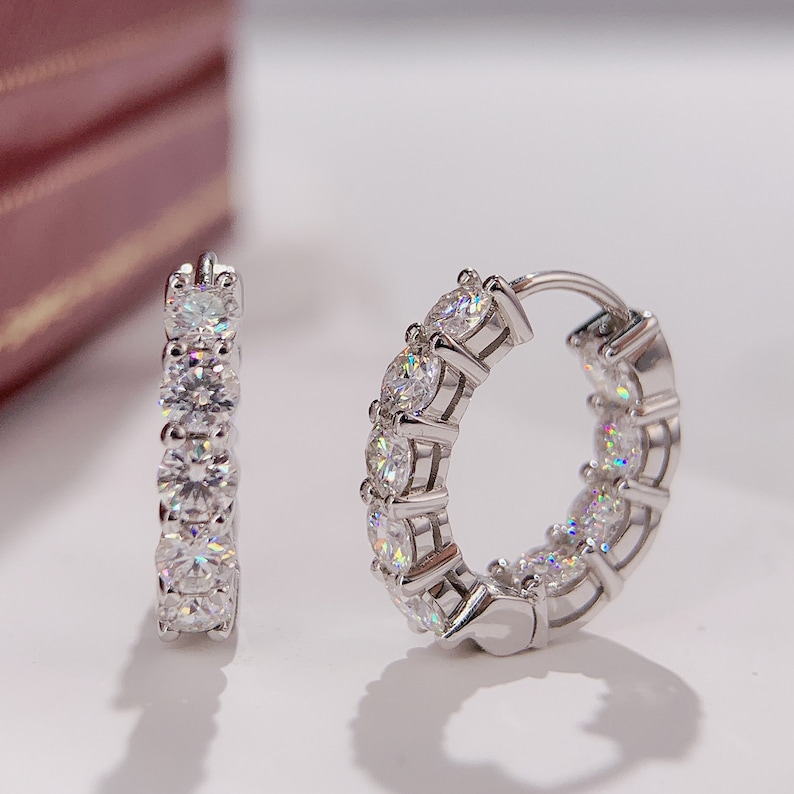 Puede incluir: Un par de pendientes de aro de plata con una fila de piedras redondas de circonita c&uacute;bica transparentes engastadas en cada aro.