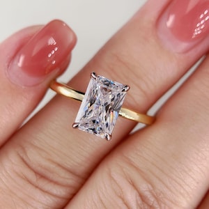 May include: A gold engagement ring with a large, rectangular, clear diamond.
