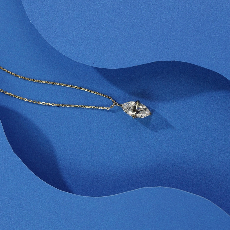 May include: A gold chain necklace with a clear marquise-shaped pendant on a blue background.