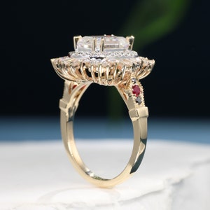 May include: A gold ring featuring a large, clear, oval-shaped centre stone surrounded by smaller diamonds. The ring has a delicate, intricate design with red and black accents.