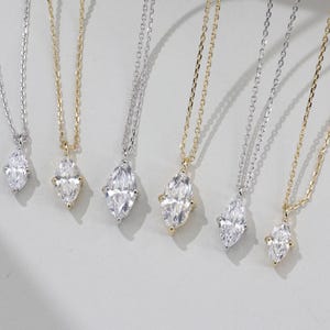 May include: Five delicate necklaces with marquise-shaped diamond pendants. The necklaces are on a white background and feature different chain styles.