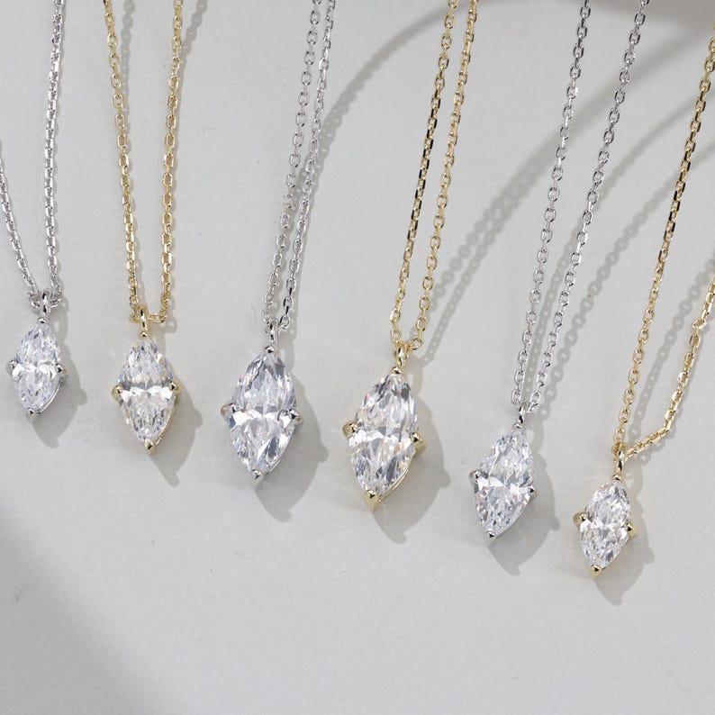 May include: Five delicate necklaces with marquise-shaped diamond pendants. The necklaces are on a white background and feature different chain styles.