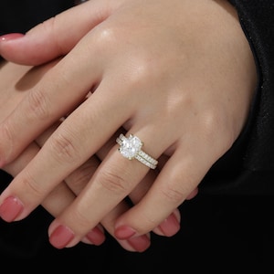 Op de afbeelding: Een close-up van een hand met een gouden verlovingsring met een grote ovale diamant en een bijpassende trouwring met kleinere diamanten.