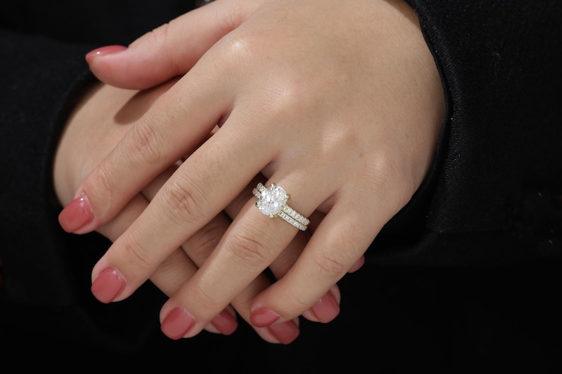 Op de afbeelding: Een close-up van een hand met een gouden verlovingsring met een grote ovale diamant en een bijpassende trouwring met kleinere diamanten.