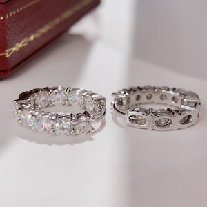 Puede incluir: Un par de pendientes de aro de plata con una fila de piedras de circonita c&uacute;bica transparentes alrededor del exterior de cada aro. Los pendientes est&aacute;n marcados con el texto "925 S925".