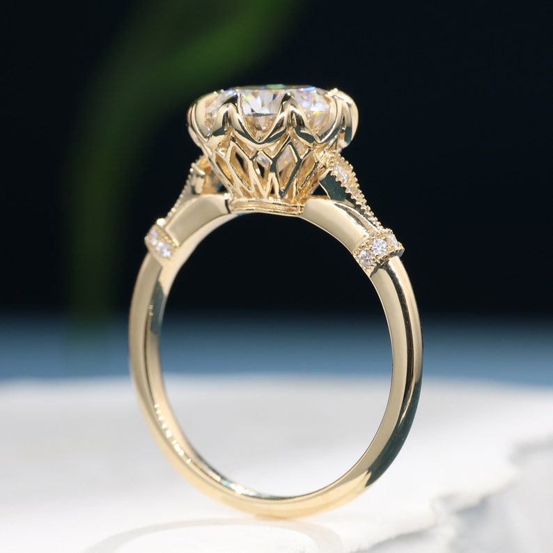 May include: A gold ring with a large, clear gemstone. The ring features intricate filigree detailing around the gemstone and small accent stones on the band. The band is a polished gold color.