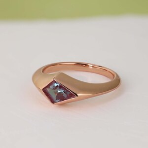 May include: Rose gold ring featuring a square-cut, color-changing gemstone. The ring has a smooth, rounded band that widens to hold the gemstone. The gemstone shifts between blue and purple hues, adding a unique touch to the jewelry.