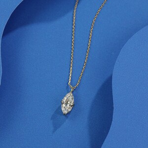 May include: A delicate gold chain necklace with a single, large, clear marquise-shaped diamond pendant.