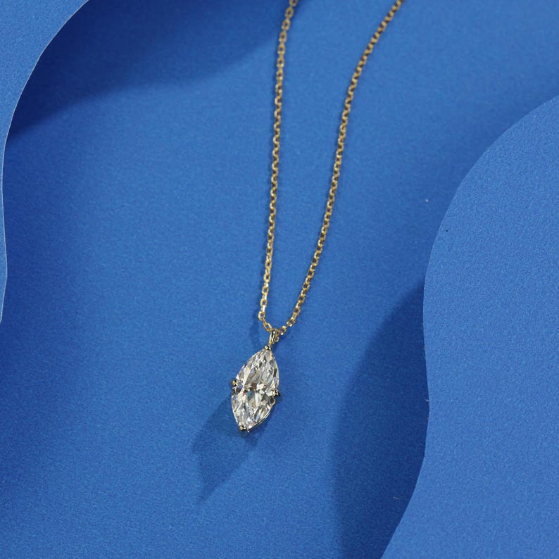 May include: A delicate gold chain necklace with a single, large, clear marquise-shaped diamond pendant.