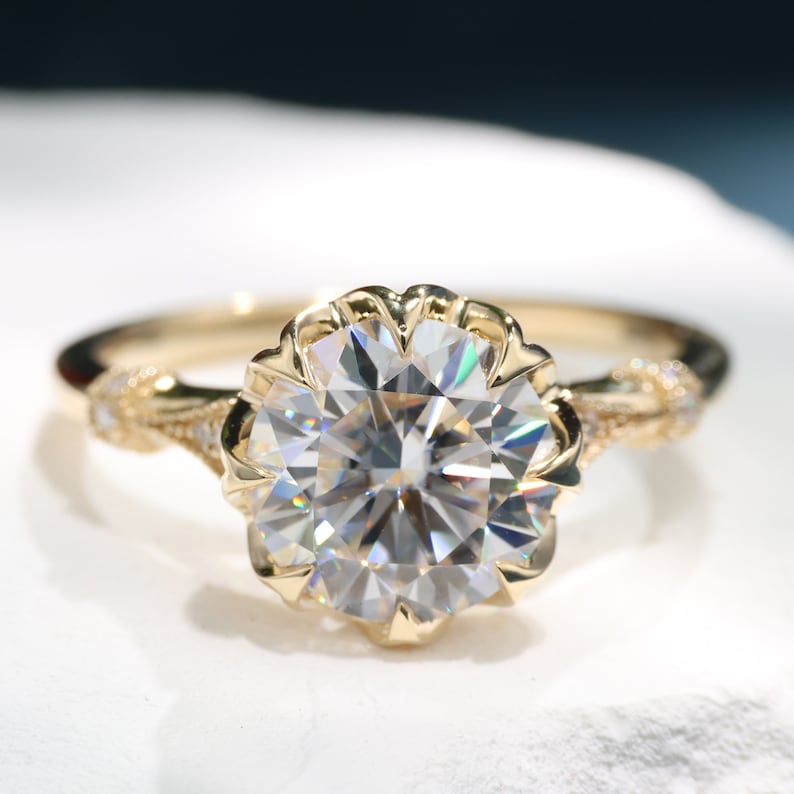 May include: A gold engagement ring with a large, round, clear gemstone. The gemstone is set in a flower-shaped setting. The band has a delicate, braided design with small accent stones.