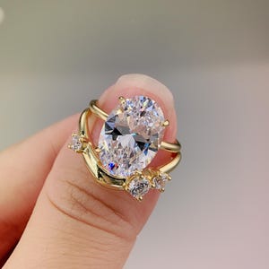 Puede incluir: Un anillo de oro con una piedra grande de forma ovalada transparente y tres piedras transparentes más pequeñas en la banda.