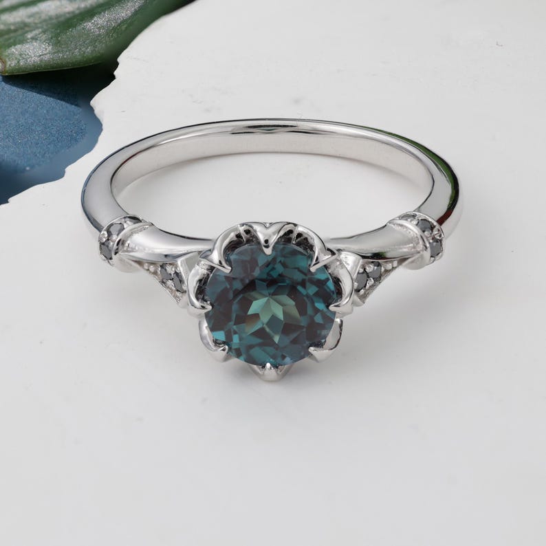 May include: A silver ring featuring a large, round, teal-colored gemstone. The gemstone is set in a floral-shaped setting. The band has decorative accents on the sides. A beautiful piece of jewelry.