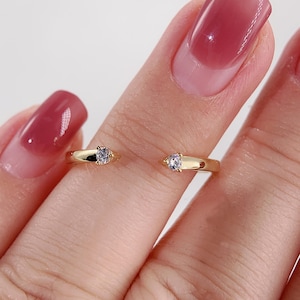 Op de afbeelding: Een gouden ring met twee kleine, heldere stenen. De ring is open en kan aan de middelvinger worden gedragen.