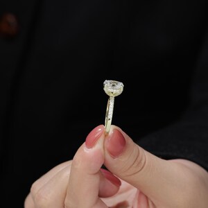 Op de afbeelding: Een gouden ring met een grote, heldere, ovale edelsteen omringd door kleinere diamanten.