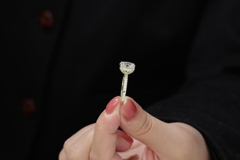 Op de afbeelding: Een gouden ring met een grote, heldere, ovale edelsteen omringd door kleinere diamanten.