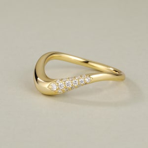 Puede incluir: Un anillo de oro con una banda ondulada y una fila de pequeños diamantes engastados en la parte superior de la banda.