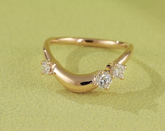 May include: A curved gold ring with three clear gemstones. The ring has a smooth, polished finish and is set against a light green background. The gemstones are evenly spaced along the curve of the ring.