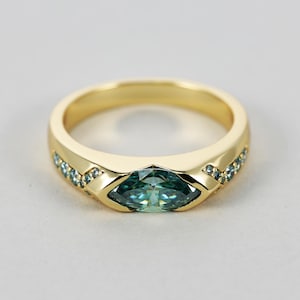 May include: A gold ring with a marquise-shaped green gemstone surrounded by smaller blue gemstones.