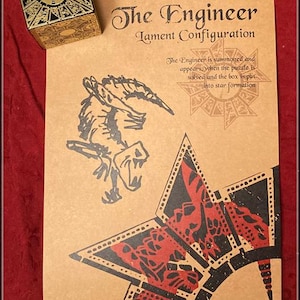 May include: A gold and black puzzle box sits beside a tan paper with the text "The Engineer, Lament Configuration". The paper features a black and red star design and a monster illustration.