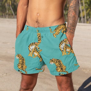 Puede incluir: Un hombre lleva puesto un bañador turquesa con un patrón repetido de tigres amarillos. El bañador tiene una cintura con cordón y un cierre de botón.