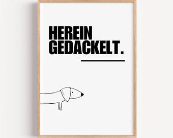 Può includere: Una stampa incorniciata con un design minimalista. La stampa presenta la frase tedesca "HEREIN GEDACKELT" in grassetto nero sopra una linea orizzontale e un semplice disegno a tratto di un cane bassotto. La cornice è di colore marrone chiaro.
