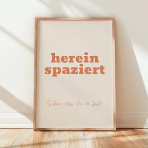 Könnte beinhalten: Ein gerahmter Druck mit dem Text "herein spaziert" in orangefarbenen Buchstaben auf weißem Hintergrund. Der Text "Schon, dass du da bist" ist darunter in Kursivschrift geschrieben.