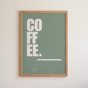 Puede incluir: Un cuadro rectangular en un marco de madera clara con un fondo verde salvia que presenta la palabra COFFEE impresa en letras mayúsculas blancas grandes apiladas verticalmente, seguida de una línea horizontal blanca debajo.