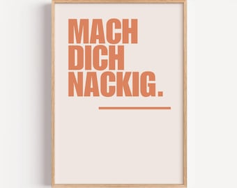 Può includere: Una stampa incorniciata con la scritta "MACH DICH NACKIG" in lettere arancioni su sfondo color pesca chiaro. Una linea orizzontale arancione sottolinea il testo. La cornice è in legno chiaro.