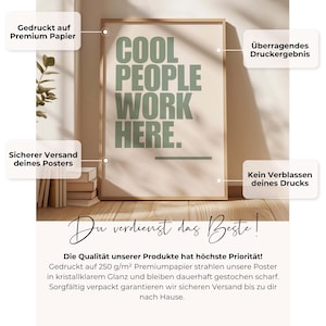 May include: A framed poster with the text "COOL PEOPLE WORK HERE" in green letters on a cream background. The poster is in a light brown frame and is displayed on a wooden surface.