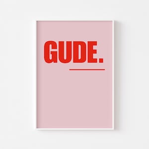 Peut inclure: Impression d'art encadrée avec le mot "GUDE" en lettres rouges audacieuses sur fond rose clair. Une ligne rouge souligne le mot. L'impression est présentée dans un cadre blanc.