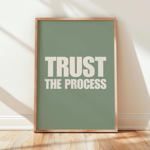 Op de afbeelding: Een ingelijst print met een saliegroene achtergrond en witte tekst die "TRUST THE PROCESS" luidt.