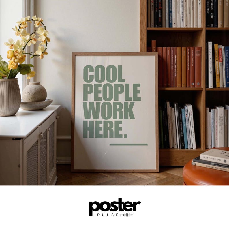 May include: A framed poster with the text "COOL PEOPLE WORK HERE" in green letters. The poster is in a room with a white cabinet, vases, and a bookshelf filled with books. The poster has a wooden frame.