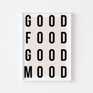 Op de afbeelding: Een wit ingelijst print met een beige achtergrond en zwarte tekst die "GOOD FOOD GOOD MOOD" luidt.