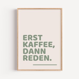 Peut inclure: Une affiche encadrée sur fond beige clair avec le texte ERST KAFFEE, DANN REDEN. imprimé en police sans-serif vert sauge. Une ligne horizontale vert sauge est située sous le texte, le tout entouré d'un cadre en bois clair.
