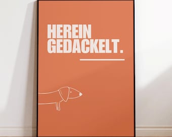 Può includere: Poster incorniciato con sfondo arancione bruciato. Il poster presenta il testo tedesco "HERIN GEDACKELT" in lettere bianche, con una linea bianca sottostante. Un disegno a tratto bianco di un bassotto è in basso.