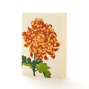 May include: A folded greeting card featuring a detailed illustration of a chrysanthemum flower. The flower is rendered in shades of orange and yellow, with green leaves and stem. The card has a cream-colored background.