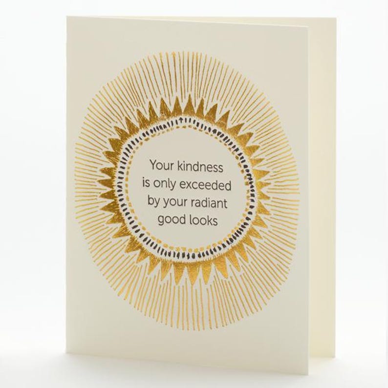 Może przedstawiać: Złożona kartka z życzeniami z kremowym tłem. Prz&oacute;d przedstawia złoty okrągły wz&oacute;r z napisem "Your kindness is only exceeded by your radiant good looks" w złotym kolorze. Wnętrze karty jest puste.