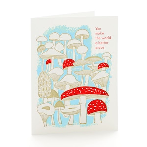 May include: Greeting card with a whimsical mushroom illustration. The design features various mushroom types in gold, red, and white against a light blue background. The text "You make the world a better place" is printed in red.