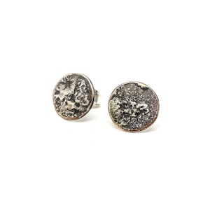 Könnte beinhalten: Ein Paar silberne Ohrstecker mit einem strukturierten, runden Design. Die Ohrringe haben eine leicht oxidierte Oberfläche, was ihnen einen antiken Look verleiht.