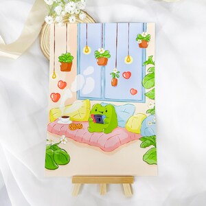 May include: A green frog wearing a pink shirt sits on a pink couch with yellow pillows. The frog is holding a video game controller. There are plants hanging from the ceiling and a window with a blue sky and white clouds in the background.