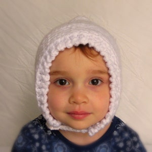 Peut inclure: Un bonnet de b&eacute;b&eacute; en crochet blanc avec un bord festonn&eacute;. Le bonnet est port&eacute; par un b&eacute;b&eacute; aux cheveux bruns et aux yeux bruns.