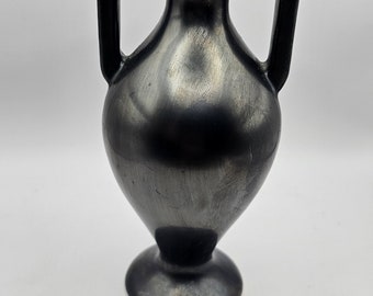 Può includere: Un vaso in ceramica nera con due manici. Il vaso ha un corpo arrotondato e una base svasata.