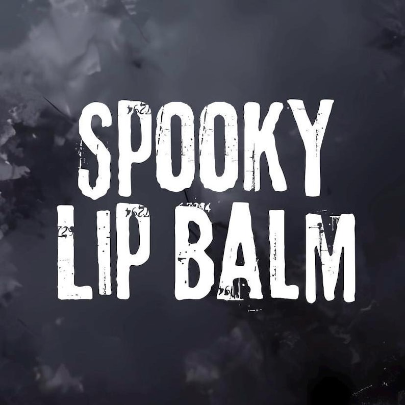 May include: White text on a dark, cloudy background reads "SPOOKY LIP BALM." The text has a distressed, textured appearance, suggesting a vintage or handmade aesthetic. The overall theme is Halloween or spooky-themed beauty products.