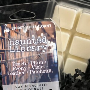 May include: A clear plastic clamshell package containing a soy blend wax melt. The label reads "Haunted Library" with scent notes. The wax melt is 2.8 ounces. The wax is a light beige color.