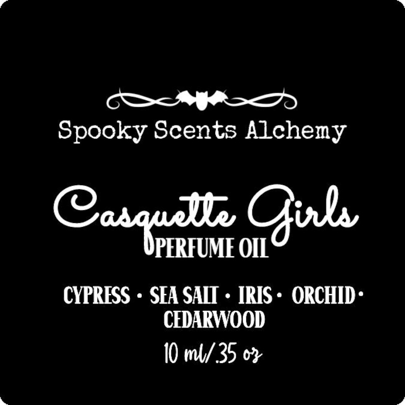 May include: Black and white label with the text "Spooky Scents Alchemy" and "Casquette Girls Perfume Oil" with a bat graphic. The label lists the fragrance notes: Cypress, Sea Salt, Iris, Orchid, Cedarwood. The label also states the volume: 10 ml / .35 oz.