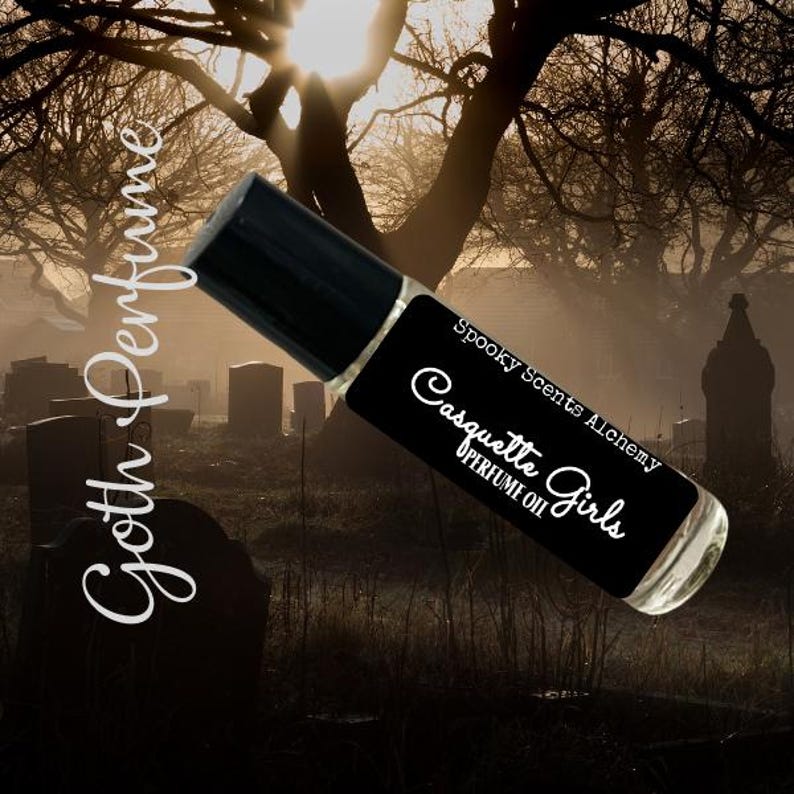 May include: A black roll-on bottle of perfume oil with the text "Spooky Scents Alchemy Casquette Girls Perfume Oil" on the label. The bottle is photographed against a dark, foggy background with trees and tombstones.