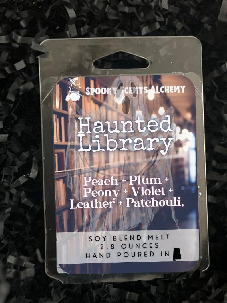 May include: A soy blend melt in a clear plastic package. The label reads "Haunted Library" with scent notes of peach, plum, peony, violet, leather, and patchouli. It weighs 2.8 ounces and is hand-poured.
