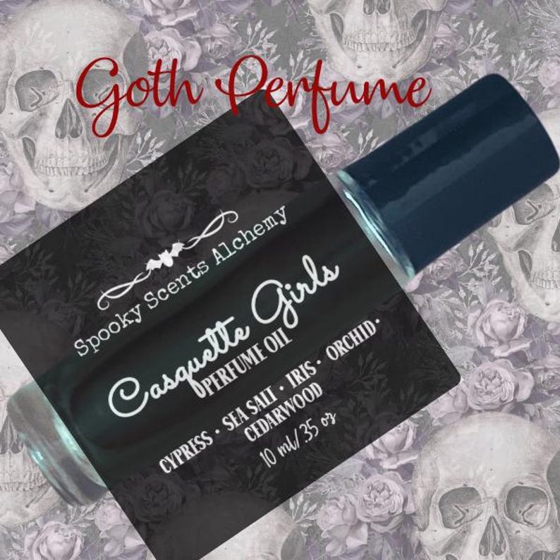May include: A black and white label with the text "Spooky Scents Alchemy Casquette Girls Perfume Oil Cypress - Sea Salt - Iris - Orchid. Cedarwood 10 ml/35 oz" on a clear glass bottle with a dark blue cap.