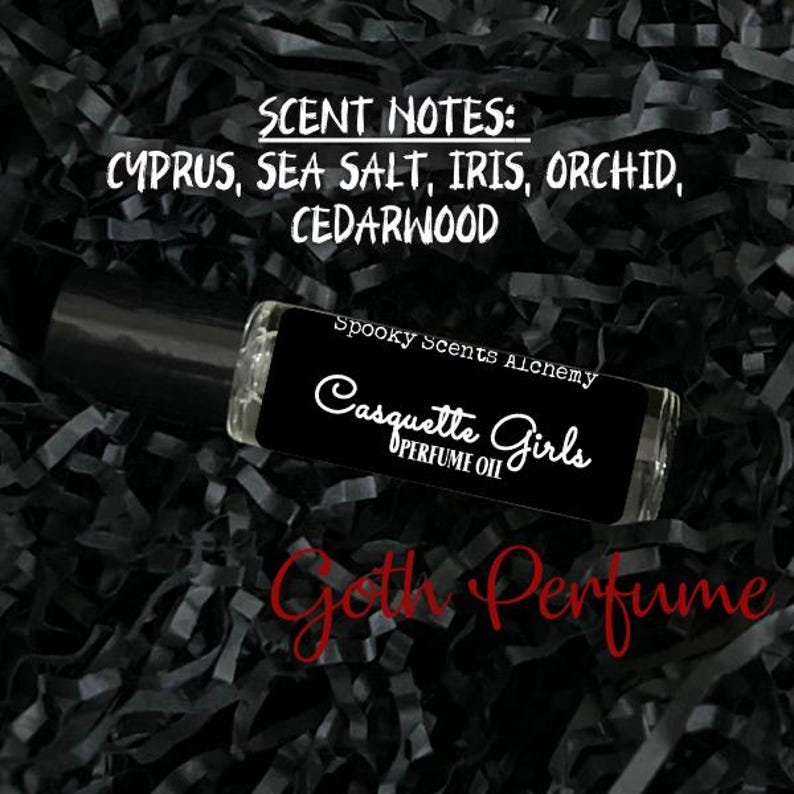 May include: A black roll-on bottle with a white label that reads "Spooky Scents Alchemy Casquette Girls Perfume Oil". The scent notes are listed as "Cyprus, Sea Salt, Iris, Orchid, Cedarwood".